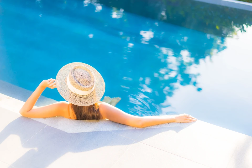 Terrasse extérieure privée avec piscine rectangulaire encastrée, deux transats blancs avec coussins beiges sur platelage bois