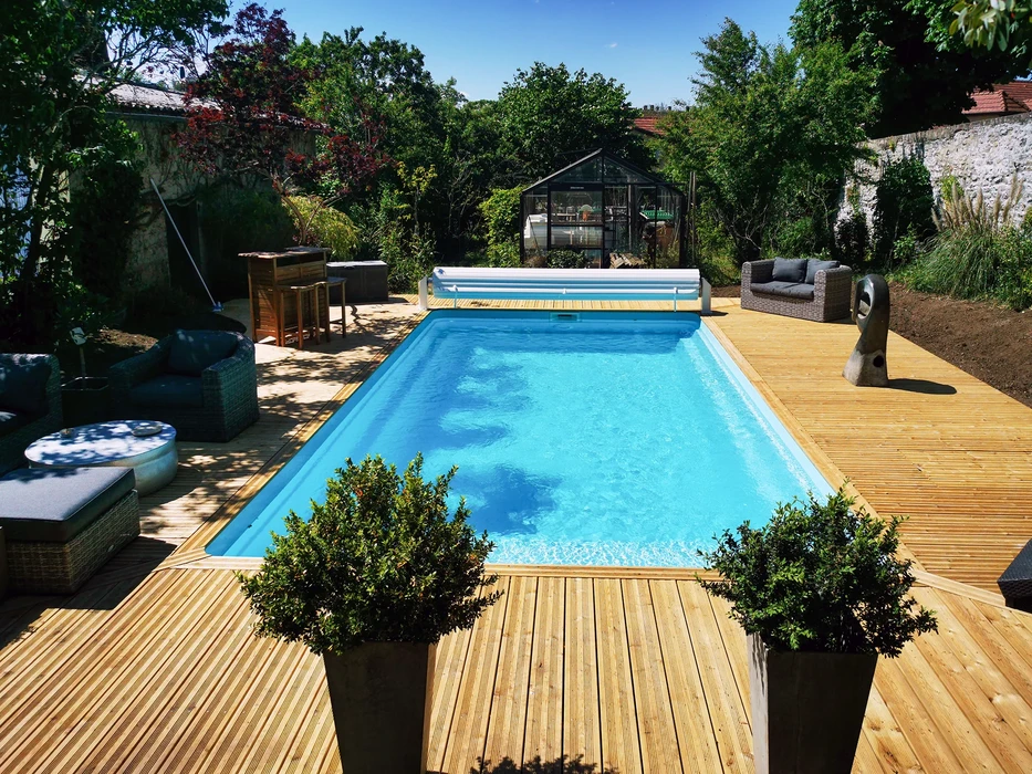 Piscine rectangulaire avec margelles en béton et plage en bois composite, située dans jardin privé avec pelouse entretenue