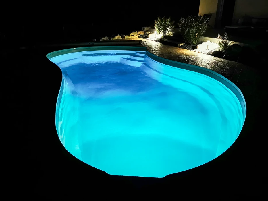 Piscine extérieure avec terrasse en bois exotique, reflet du soleil sur l'eau bleue cristalline