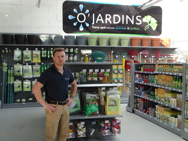 Fleuriste souriante en tablier beige tenant un bouquet de tulipes roses devant sa boutique